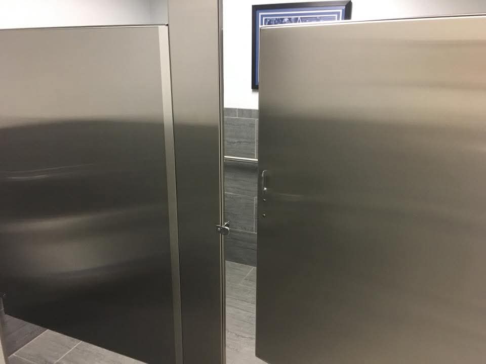 Brushed stainless steel bathroom stall partitions in a modern restroom with grey tiled walls.