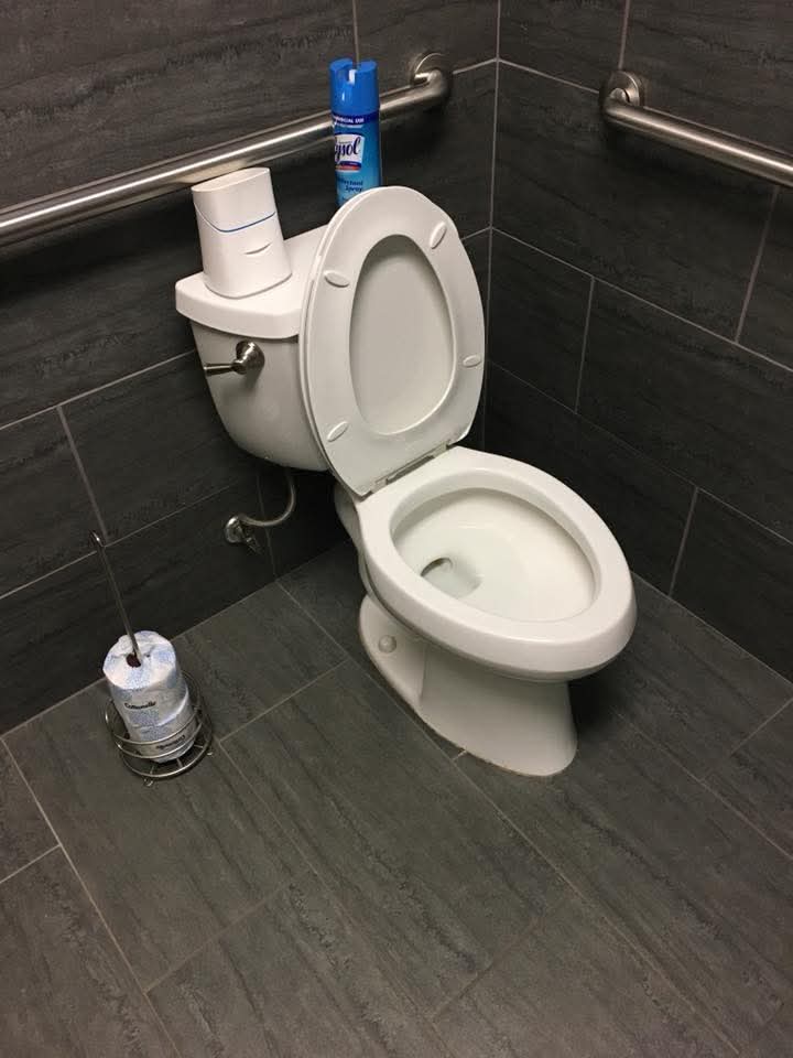 White toilet with seat up, Lysol spray on tank, in a dark gray tiled bathroom.